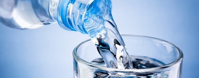 Pouring water from bottle into glass on blue background